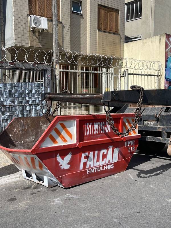 Caçamba vermelha sendo posicionada pelo caminhão na rua